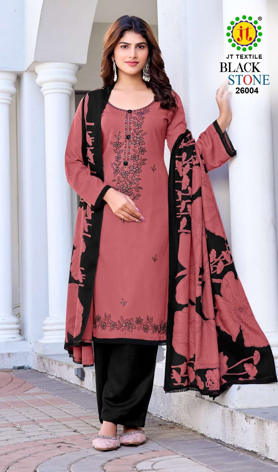 Woman wearing a pink and black embroidered outfit with a white architectural background | JT TEXTILE BLACK STONE VOL-26 26001 TO 26005 SERIES PURE RAYON EMBROIDERY PAKISTANI DRESSES