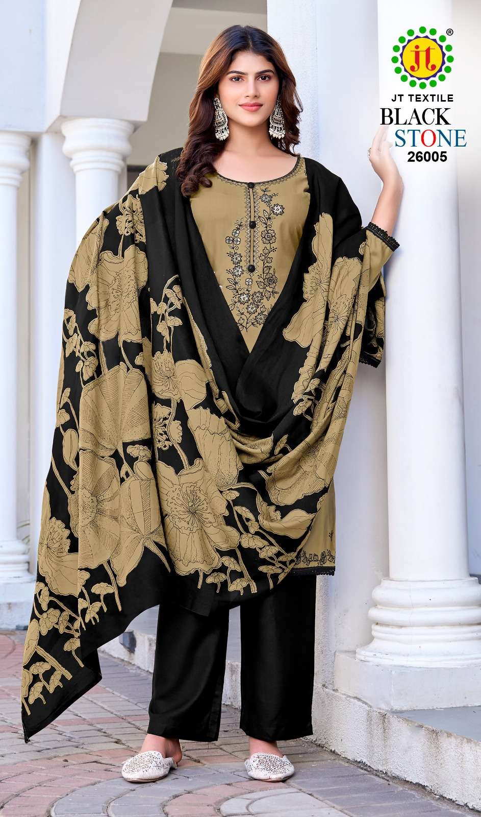 Woman wearing a black and gold traditional outfit with a text overlay on a white architectural background | JT TEXTILE BLACK STONE VOL-26 26001 TO 26005 SERIES PURE RAYON EMBROIDERY PAKISTANI DRESSES
