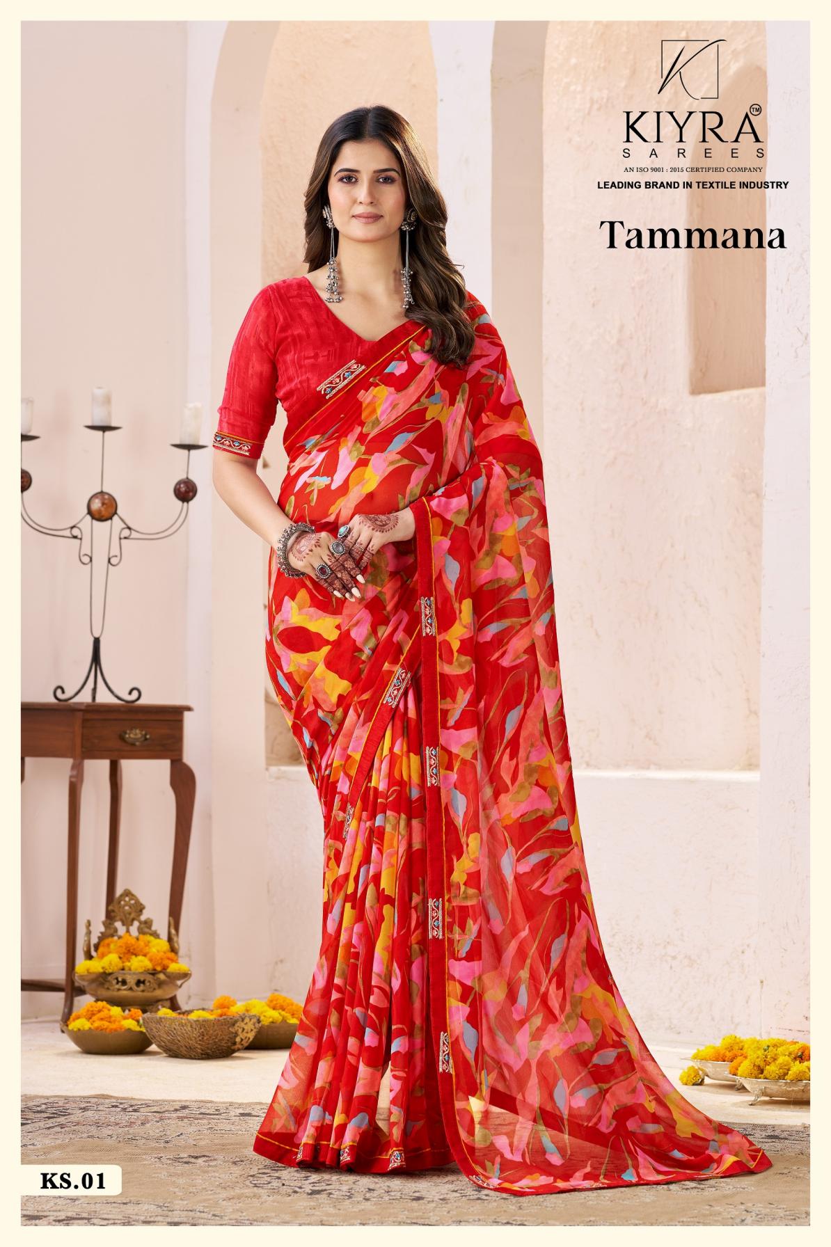 Woman wearing a red saree with floral patterns in a decorated room. | Kiyra Presents Tammana Georgette Fancy Sarees