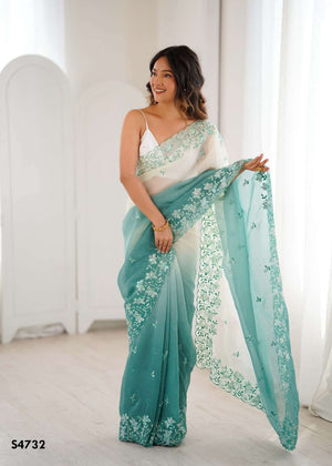 Woman wearing a teal saree with white embroidery in a bright room.
