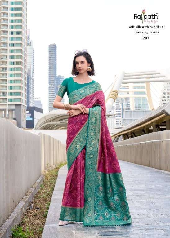Woman in a green and pink saree standing on a bridge with cityscape in the background | RAJPATH Sugandh Silk Pure Silk Bandhani Sarees Catalogue