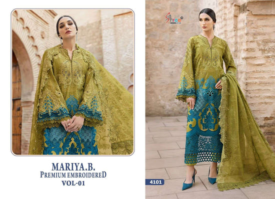 Woman wearing a green and blue embroidered outfit with a brick wall background | SHREE FAB MARIA B VOL-01 Pure Cotton Embroidered Pakistani Dresses Wholesale