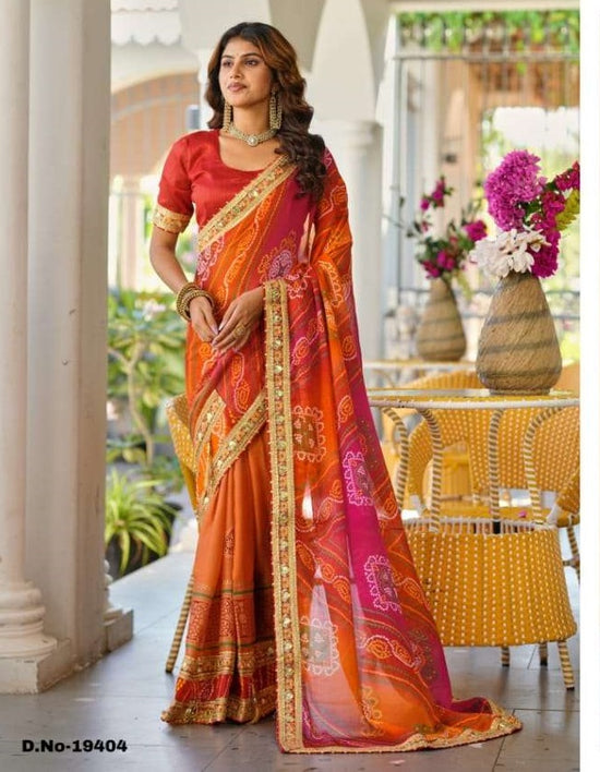 Woman wearing a vibrant orange and pink saree with a blurred indoor background | SWARNA 19401 TO 19405 SERIES PURE CHIFFON EMBROIDERY SAREES