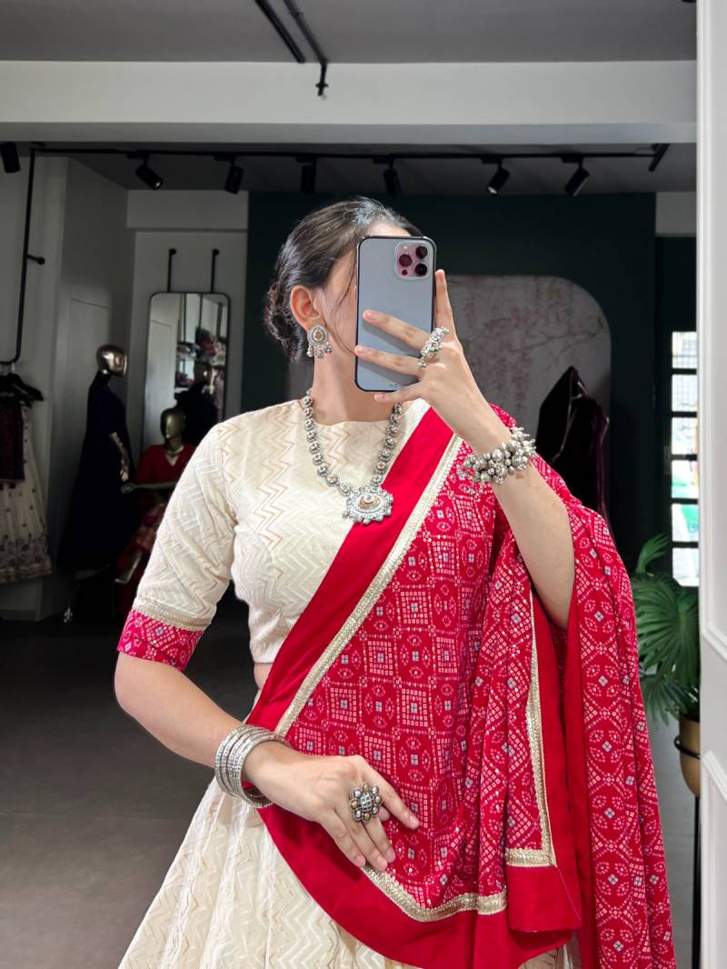 Person wearing a red and white saree with jewelry indoors. | Taraa L 1669 Cotton Bandhani Printed Fancy Lehenga Choli Collection