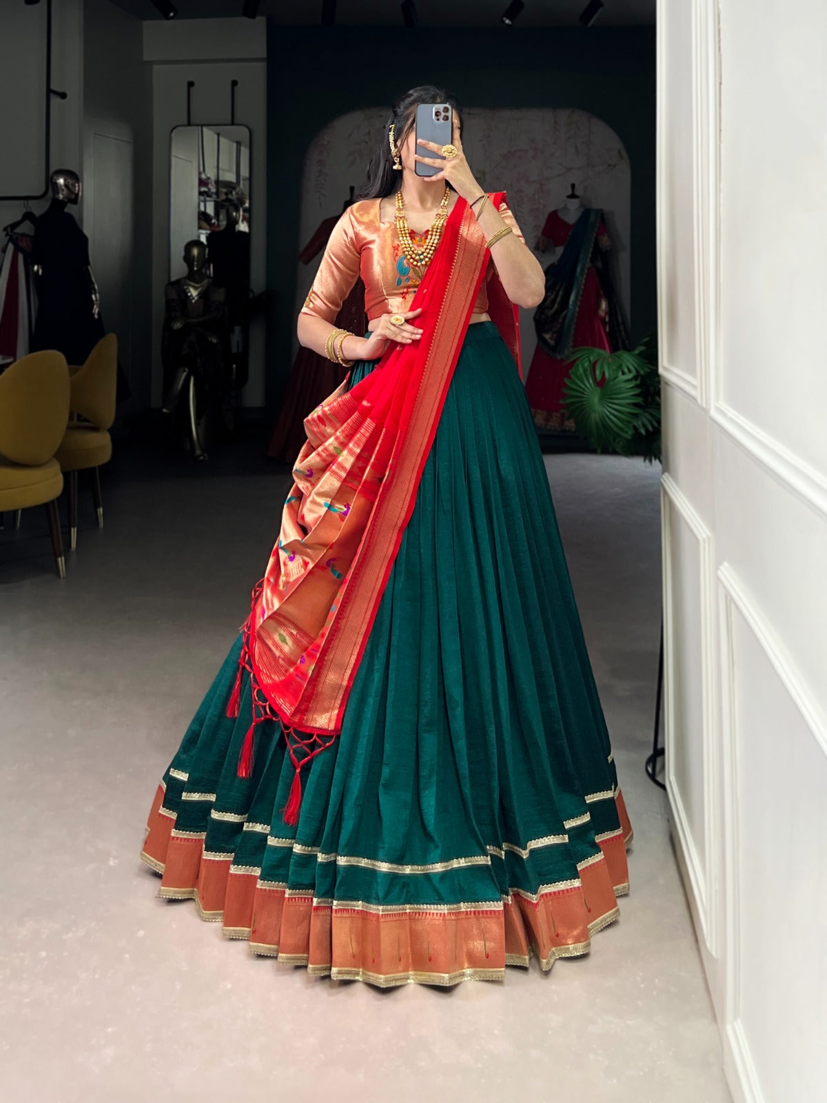 Person wearing a traditional green and red saree in a room with mirrors and chairs. | Taraa L 2007 Vichitra Silk Zari Weaving Plain Lehenga Choli Collection