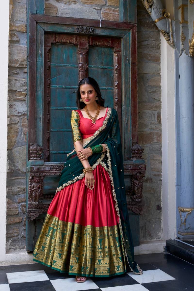 Woman in a traditional red and green saree standing in front of a decorative door. | Taraa L 2023 Narayan Pattu Zari Worked Designer Lehenga Choli Collection