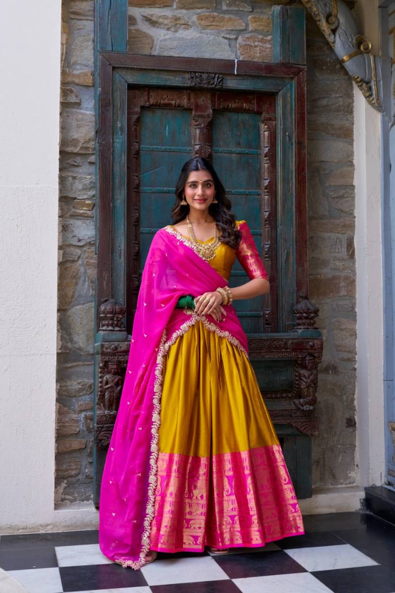 Woman in a pink and yellow traditional outfit standing in front of a decorative door. | Taraa L 2023 Narayan Pattu Zari Worked Designer Lehenga Choli Collection