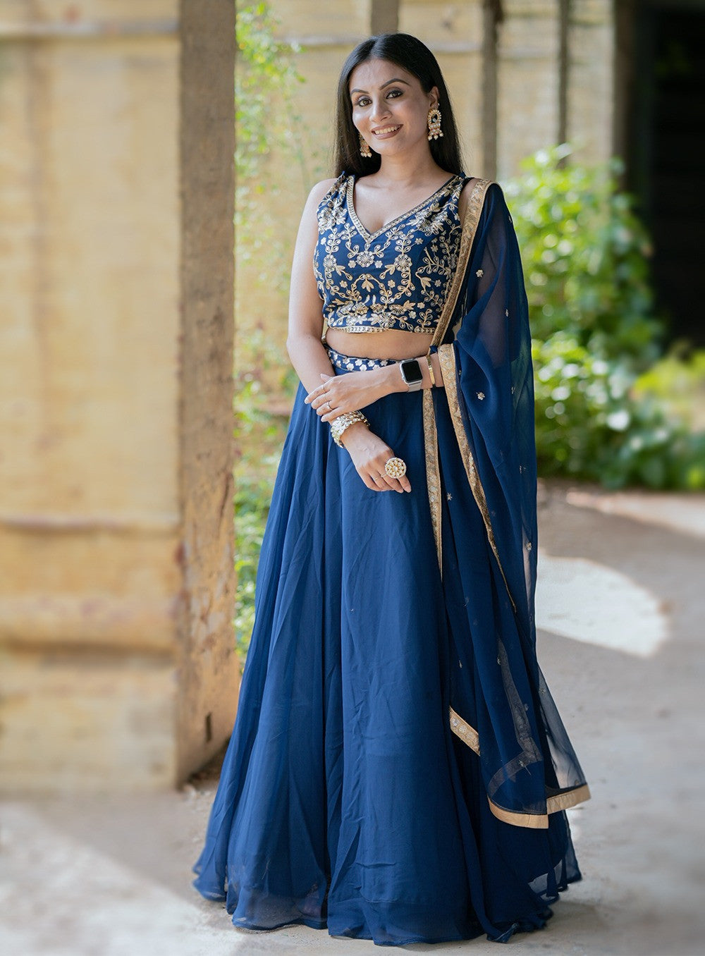 Woman in a traditional blue outfit with gold details standing outdoors.| V3 366 Faux Georgette Embroidered Designer Lehenga Choli Wholesale Price
